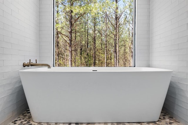 bathroom with a washtub, a wealth of natural light, and tile walls