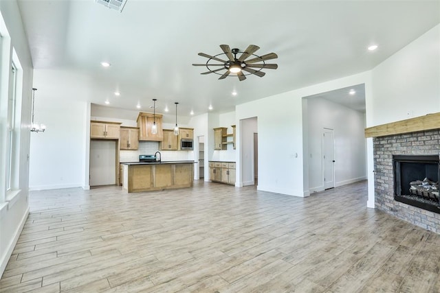 living room featuring a fireplace, light wood-type flooring, ceiling fan with notable chandelier, and sink