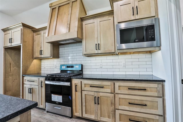 kitchen with custom exhaust hood, backsplash, light hardwood / wood-style flooring, dark stone countertops, and appliances with stainless steel finishes