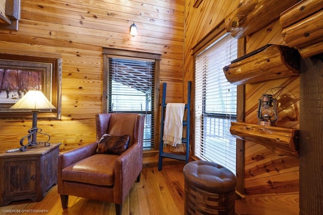 sitting room with lofted ceiling, wooden walls, light hardwood / wood-style flooring, and a healthy amount of sunlight