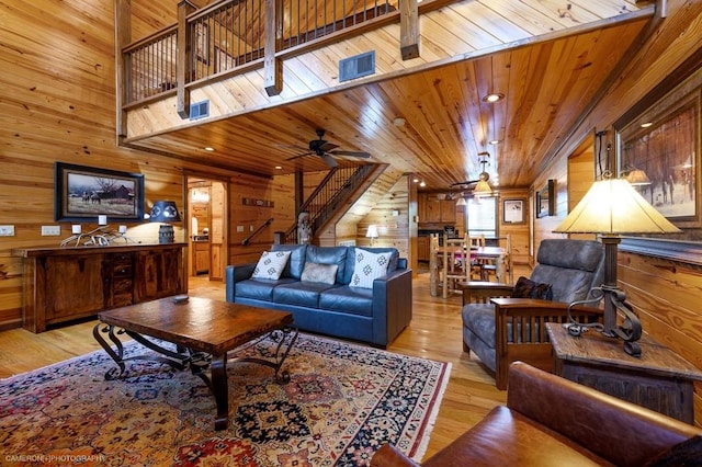 living room with light wood-type flooring, wood ceiling, ceiling fan, and wood walls