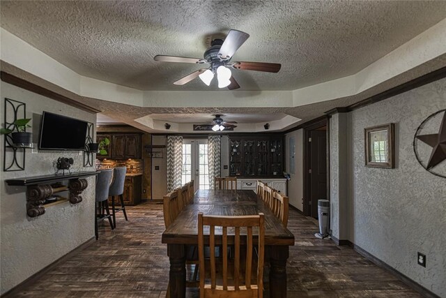 dining space with a textured ceiling, dark hardwood / wood-style flooring, a tray ceiling, and ceiling fan