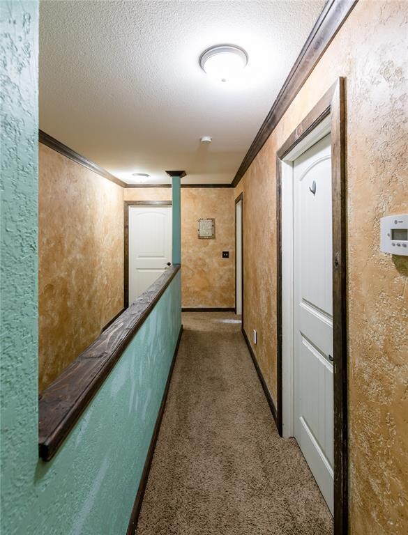 hallway featuring crown molding, a textured ceiling, and dark colored carpet