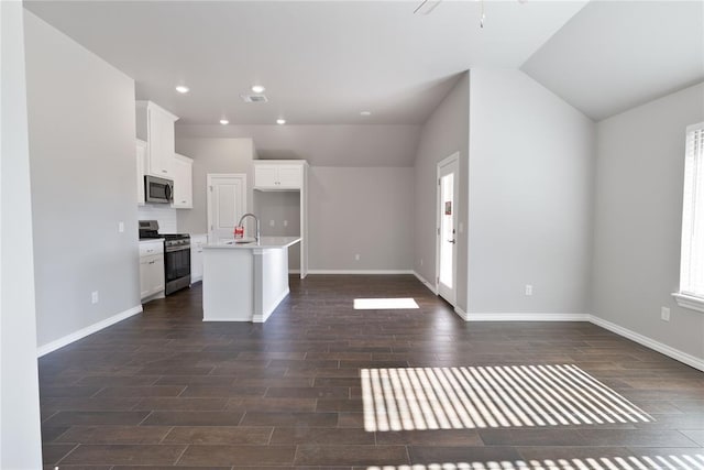 kitchen with stainless steel appliances, vaulted ceiling, white cabinetry, and an island with sink