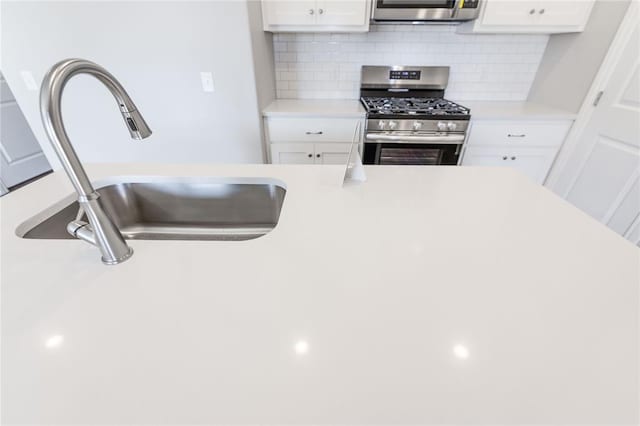 kitchen with gas stove, decorative backsplash, white cabinetry, and sink