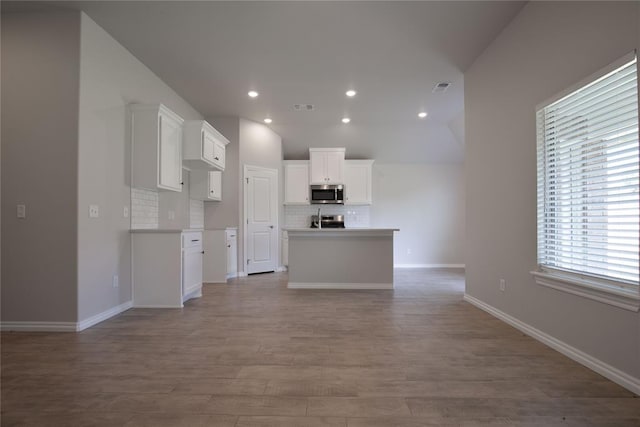 kitchen featuring white cabinetry, backsplash, vaulted ceiling, a kitchen island with sink, and appliances with stainless steel finishes