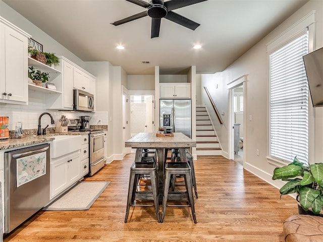 kitchen with a breakfast bar, white cabinets, stainless steel appliances, and light hardwood / wood-style floors