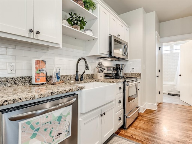 kitchen featuring light stone countertops, backsplash, appliances with stainless steel finishes, white cabinets, and light wood-type flooring