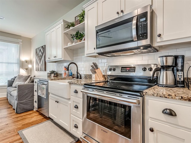 kitchen featuring appliances with stainless steel finishes, light wood-type flooring, tasteful backsplash, sink, and white cabinetry