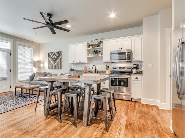 kitchen with ceiling fan, stainless steel appliances, a kitchen breakfast bar, light hardwood / wood-style floors, and white cabinets