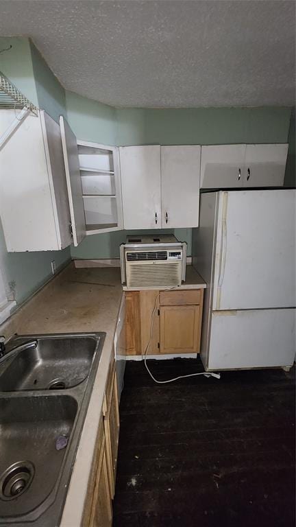 kitchen with sink, dark hardwood / wood-style floors, an AC wall unit, white fridge, and white cabinets