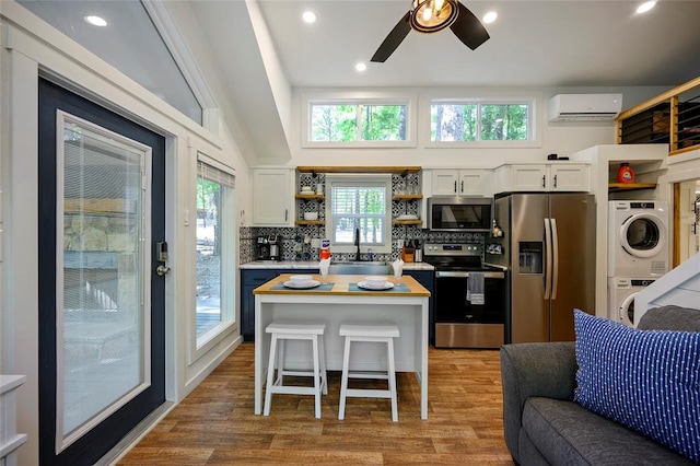 kitchen with a wall mounted air conditioner, a breakfast bar area, stacked washing maching and dryer, white cabinetry, and stainless steel appliances