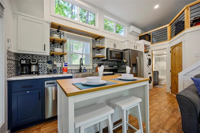 kitchen with appliances with stainless steel finishes, an AC wall unit, white cabinets, butcher block countertops, and stacked washer / drying machine