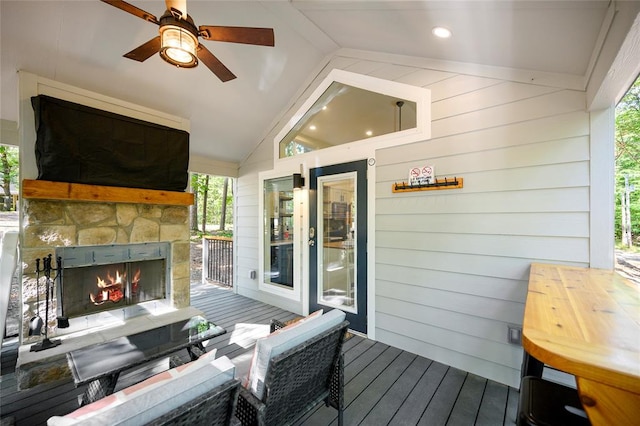 wooden deck with an outdoor stone fireplace and ceiling fan