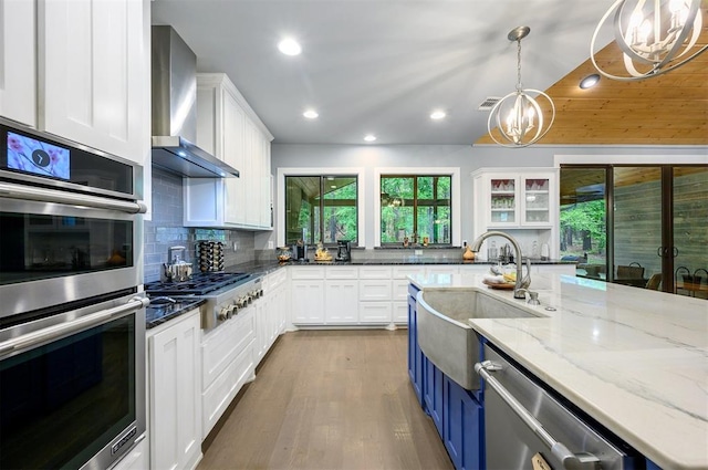 kitchen featuring white cabinetry, wall chimney exhaust hood, stainless steel appliances, dark stone countertops, and pendant lighting