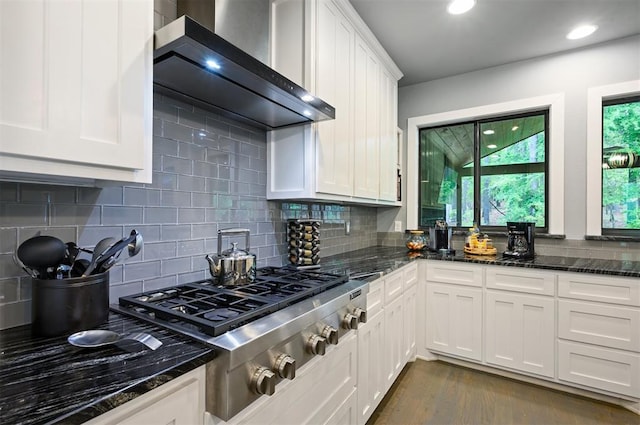 kitchen with white cabinetry, wall chimney range hood, dark stone counters, stainless steel gas stovetop, and decorative backsplash