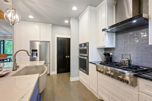 kitchen featuring backsplash, dark stone counters, wall chimney exhaust hood, stainless steel appliances, and hanging light fixtures