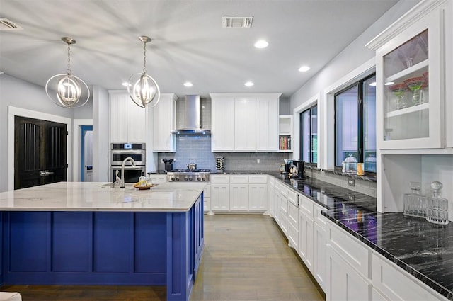 kitchen with pendant lighting, wall chimney exhaust hood, white cabinets, and dark stone counters