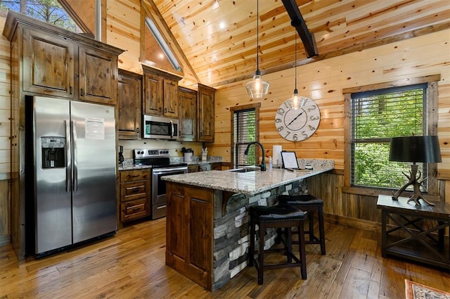 kitchen with light stone countertops, appliances with stainless steel finishes, vaulted ceiling with beams, and wood walls