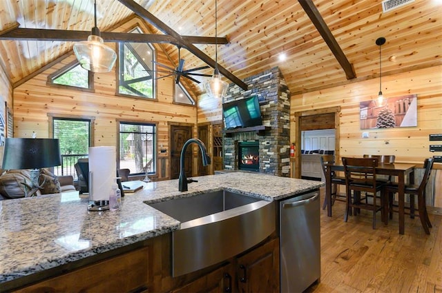 kitchen featuring pendant lighting, stone countertops, high vaulted ceiling, dishwasher, and wood walls