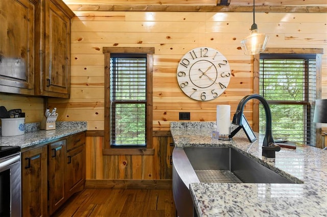 kitchen with light stone counters, a wealth of natural light, dark wood-type flooring, and wood walls