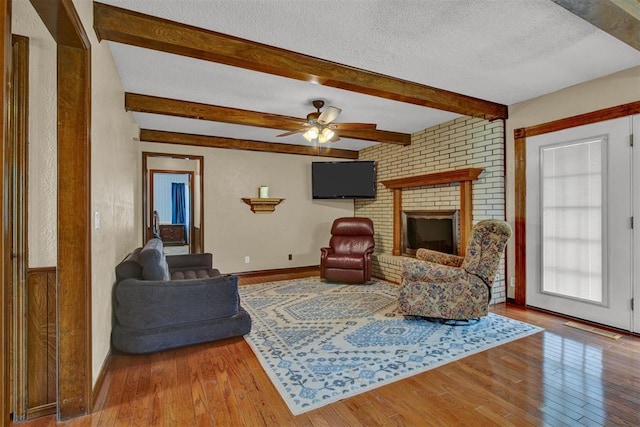 living room with beam ceiling, ceiling fan, a textured ceiling, a fireplace, and hardwood / wood-style flooring