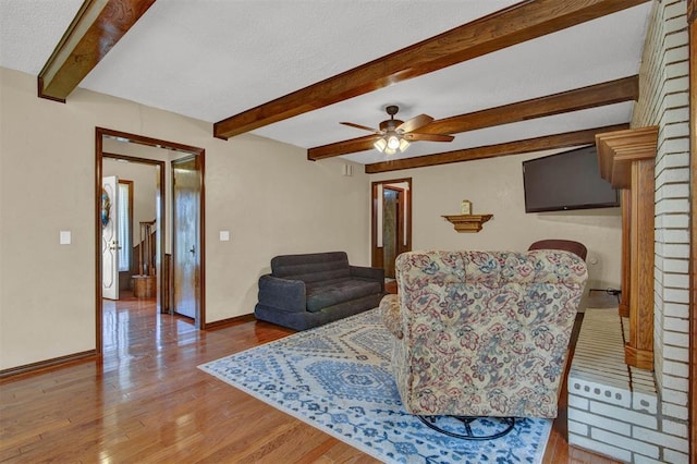 living room with a fireplace, ceiling fan, light hardwood / wood-style flooring, and beamed ceiling