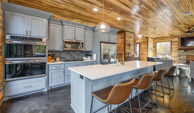 kitchen featuring appliances with stainless steel finishes, backsplash, a breakfast bar, hanging light fixtures, and wood walls