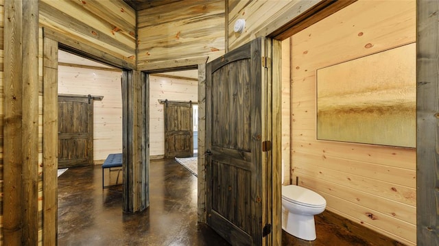 bathroom with concrete floors, toilet, and wooden walls