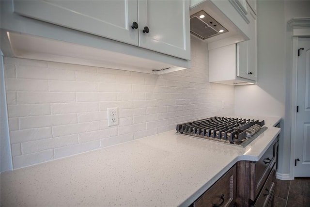 kitchen with custom exhaust hood, decorative backsplash, white cabinetry, dark brown cabinetry, and stainless steel gas cooktop