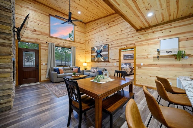 dining space featuring wooden walls, ceiling fan, wood ceiling, and a high ceiling