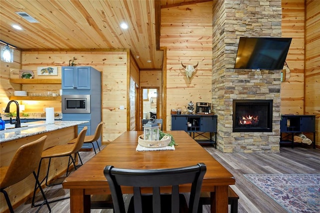 dining space with hardwood / wood-style flooring, wood walls, a stone fireplace, and wooden ceiling