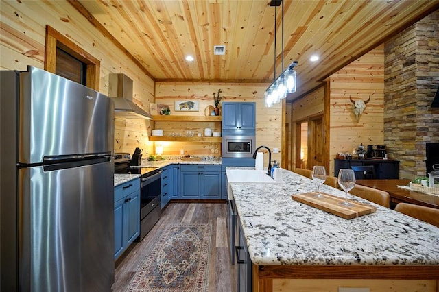 kitchen featuring wooden ceiling, wall chimney range hood, an island with sink, wooden walls, and appliances with stainless steel finishes