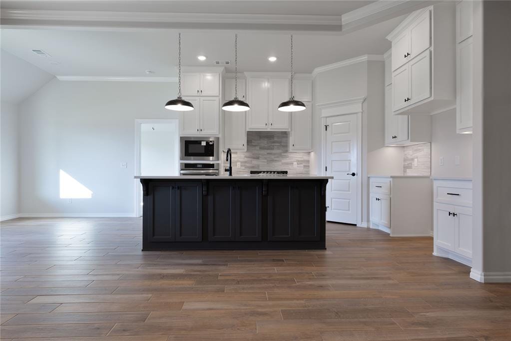 kitchen featuring appliances with stainless steel finishes, decorative light fixtures, white cabinetry, and an island with sink