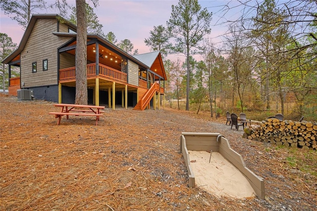 back house at dusk with ceiling fan, an outdoor fire pit, and central air condition unit