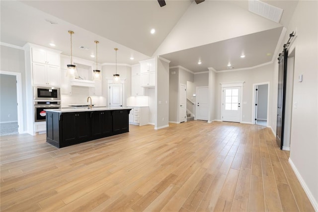 kitchen featuring a center island with sink, pendant lighting, stainless steel appliances, a barn door, and white cabinets