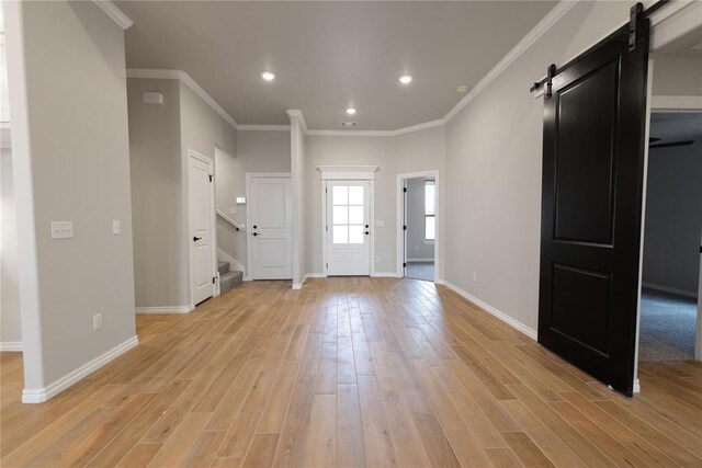 foyer with ornamental molding, a barn door, and light hardwood / wood-style floors