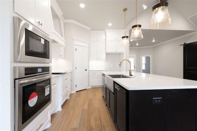 kitchen with decorative light fixtures, black microwave, white cabinets, oven, and a center island with sink