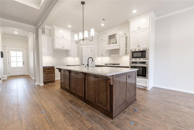 kitchen with an island with sink, dark hardwood / wood-style flooring, ornamental molding, a notable chandelier, and stainless steel appliances