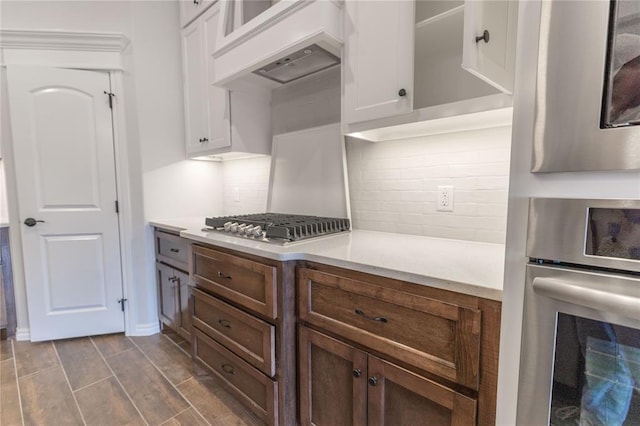 kitchen featuring white cabinetry, stainless steel appliances, tasteful backsplash, dark brown cabinetry, and custom range hood