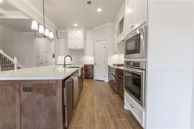 kitchen featuring white cabinetry, stainless steel appliances, decorative light fixtures, and a center island with sink