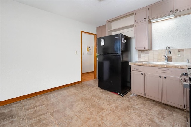 kitchen featuring tile counters, decorative backsplash, black fridge, and sink