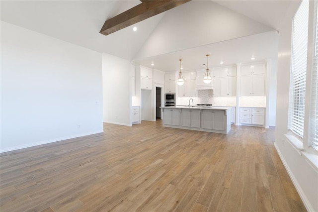 kitchen featuring high vaulted ceiling, stainless steel appliances, a sink, white cabinetry, and light wood finished floors