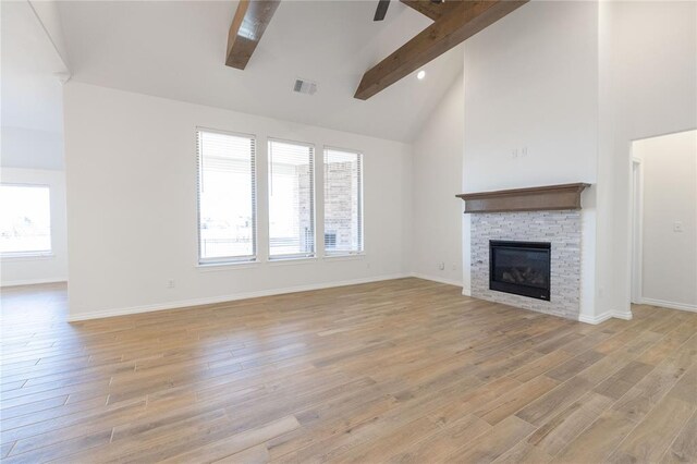 unfurnished living room featuring high vaulted ceiling, beamed ceiling, a fireplace, and light wood-style flooring