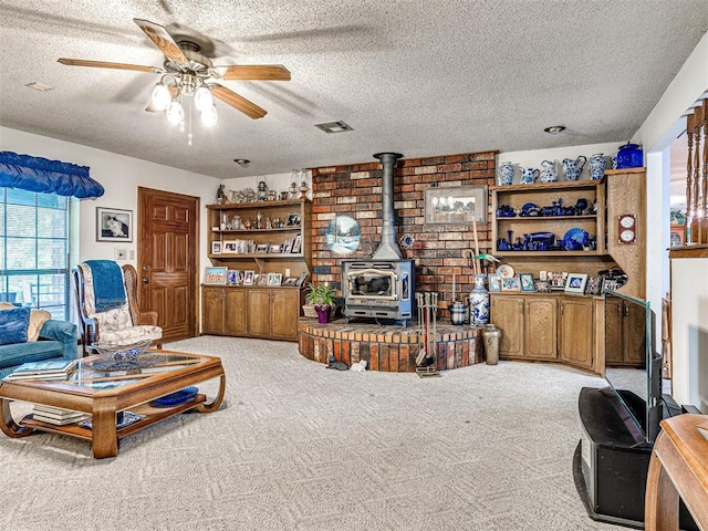 carpeted living room with ceiling fan, a wood stove, a textured ceiling, and a wealth of natural light