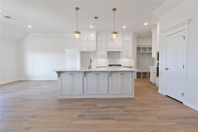 kitchen featuring white cabinets, pendant lighting, and an island with sink