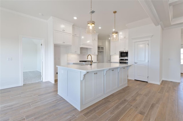 kitchen featuring pendant lighting, a center island with sink, white cabinetry, and stainless steel appliances