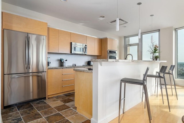 kitchen featuring a breakfast bar, appliances with stainless steel finishes, light brown cabinets, and decorative light fixtures