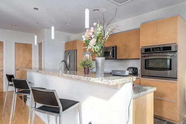 kitchen with pendant lighting, light hardwood / wood-style flooring, appliances with stainless steel finishes, light stone counters, and a breakfast bar area