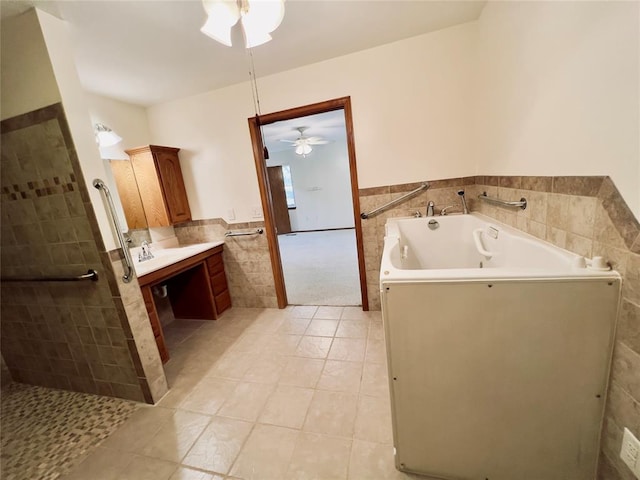 bathroom featuring ceiling fan, tile patterned floors, a tub to relax in, vanity, and tile walls